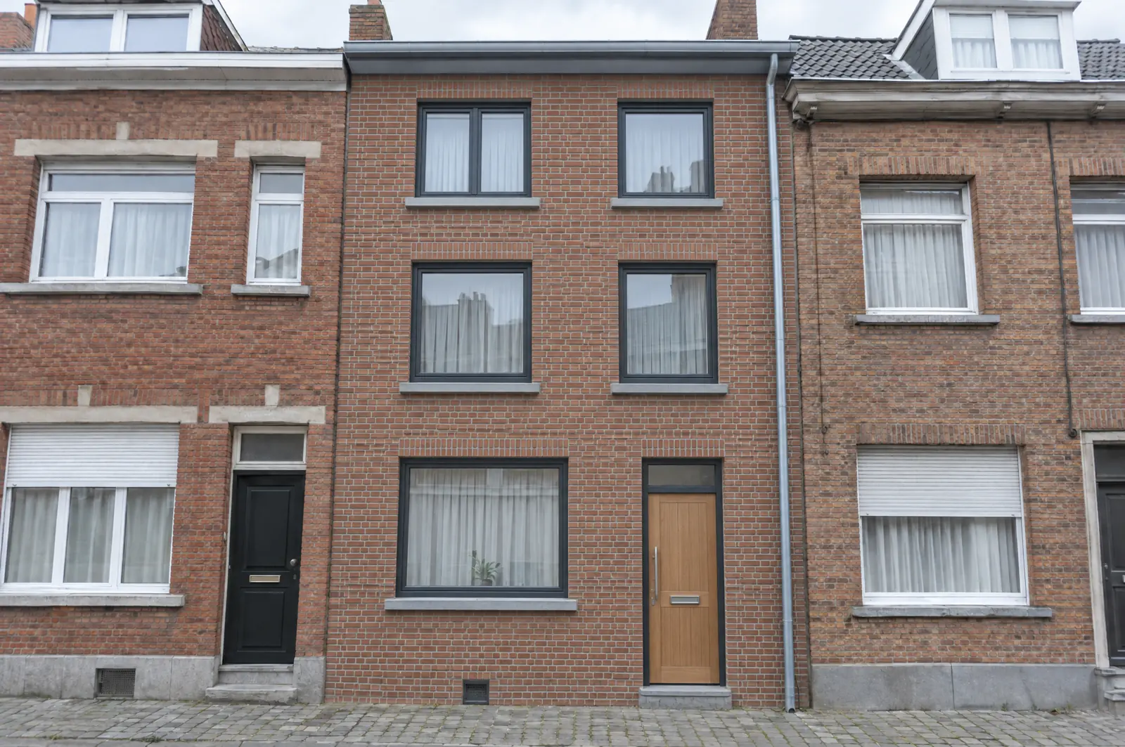 La même façade après rénovation : briques nettoyées et rejointoyées, châssis aluminium anthracite, porte en chêne