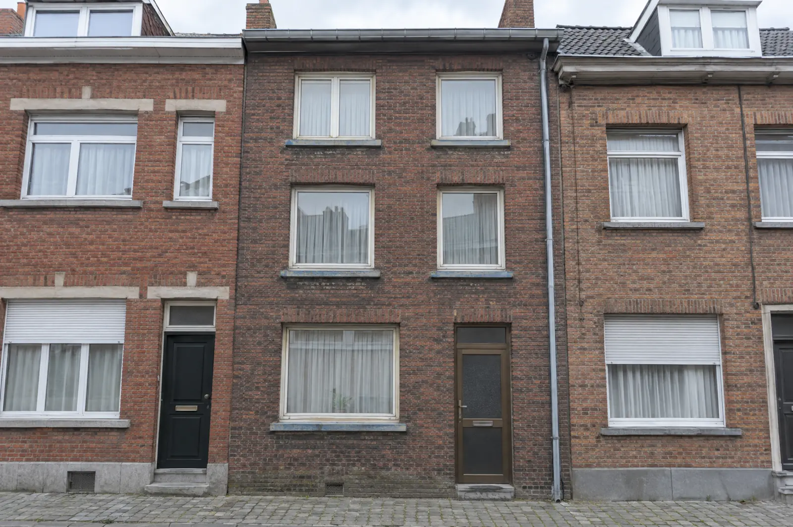 Façade de maison bruxelloise avant rénovation : briques encrassées, châssis PVC des années 80, porte en aluminium